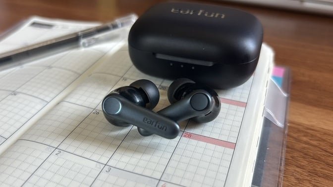 black earfun air pro 4 earbuds and case on top of open planner
